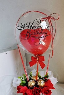 Red heart balloon stuffed inside a clear balloon tied with red riboons to a basket of 3 Ferrero and 3 red roses