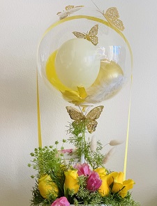 Clear balloon stuffed with yellow white balloons and 12 pink yellow roses in a basket