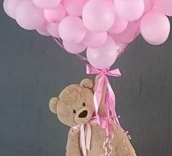 10 Pink gas pre filled balloons tied to the hand of a 12 inched brown Teddy bear